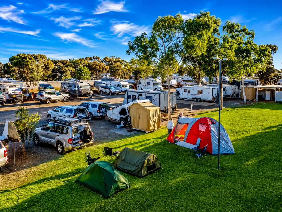Sunlit Australian caravan park with caravans, tents and gum trees under a blue sky